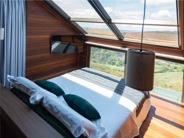 Cama sob a claraboia da Cabana Marama, com almofadas verdes e a vista das montanhas ao amanhecer