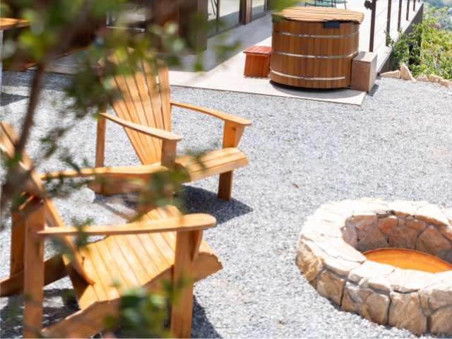 Fogueira de pedra, cadeiras de madeira e ofurô no deck externo da cabana