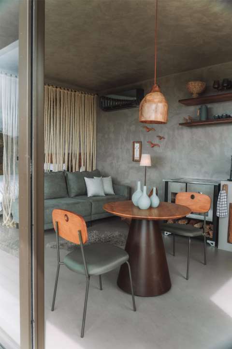 Sala da Cabana Huna com sofá verde, mesa redonda de madeira e telão de projeção na parede